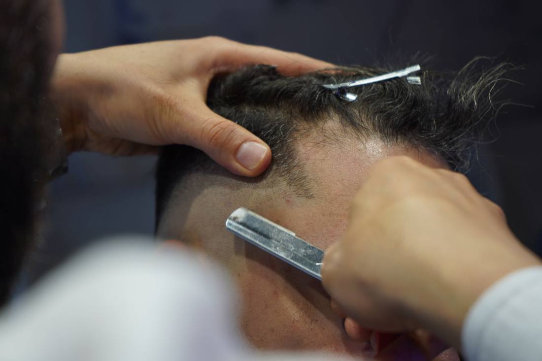 Detailed close-up of a barber using a sharp blade to shave a client's head in a salon.